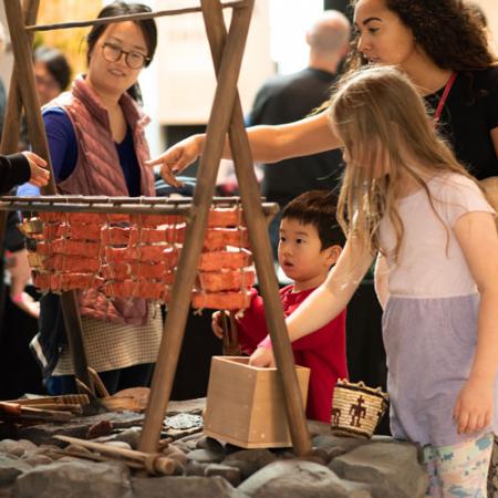 a family touches an interactive depicting salmon cooking over a fire pit