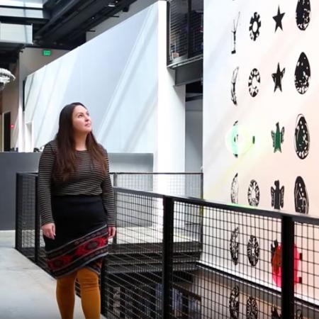 A woman stands next to a large, graphic mural she created for display in a museum