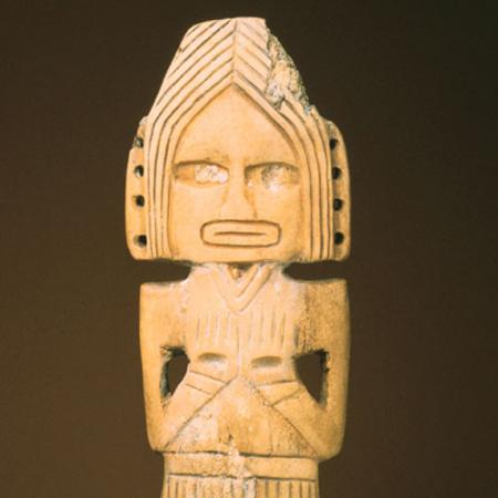 A carved figure with its arms crossed and wearing a headdress