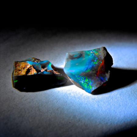 Two multi-colored rough opals sit on a table
