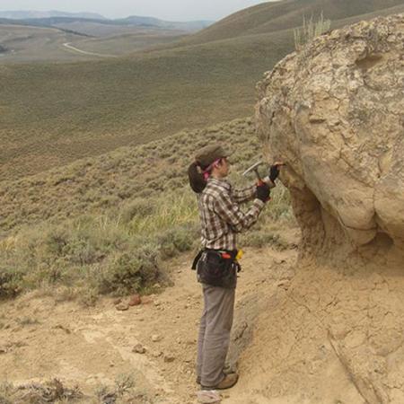 a woman reaches up to reove a sample from a rock outcrop