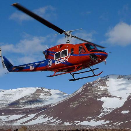 A helicopter takes off with the barren Antarctic skyline in the background