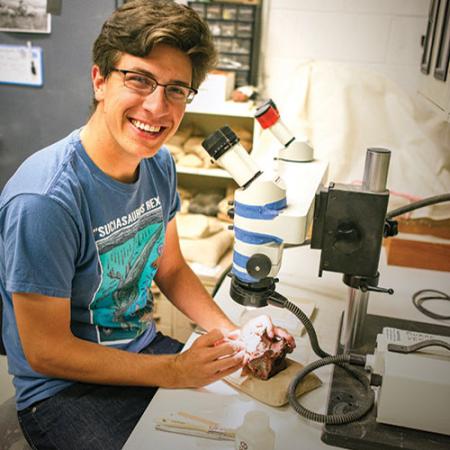 a young man uses a miniature jackhammer to remove rock from washington's first dinosaur fossil