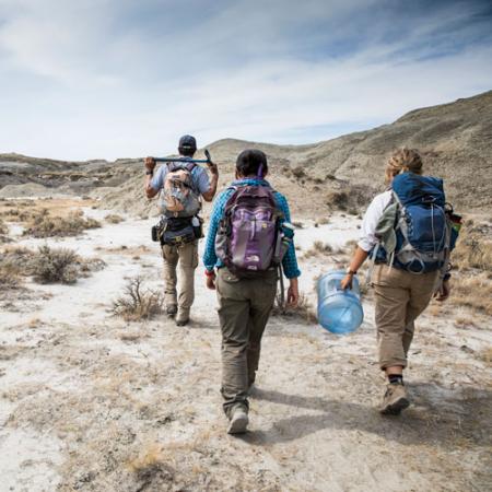 Three people with backpacks and palentology equipment walking in the desert