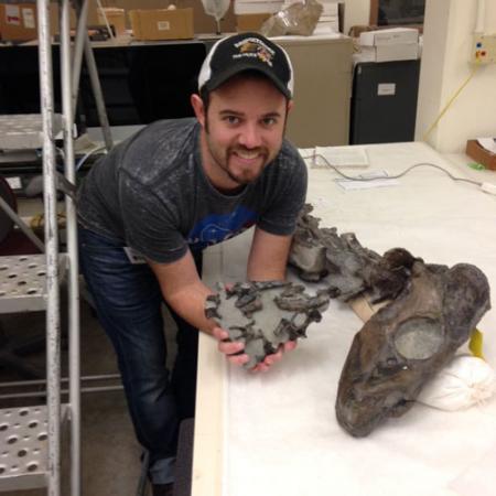 young man holds a fossil bed while crouching next to the skull of a prehistoric seal