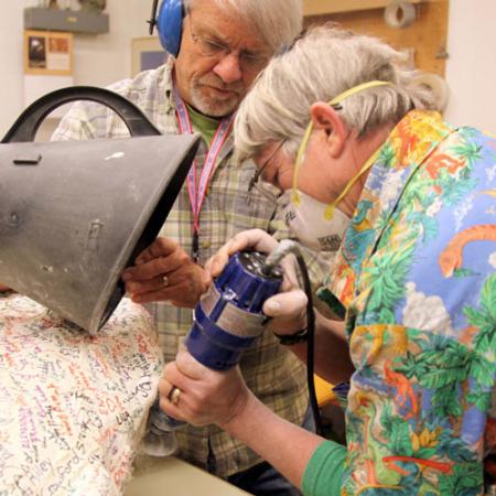 Two researchers use hand tools to cut into a plaster cast