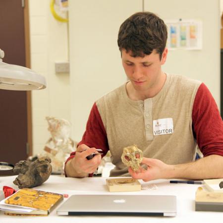 a young man holds a skull while taking measurements of the fossils