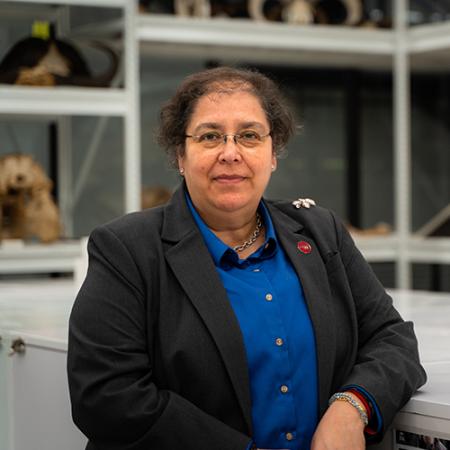 a woman smiles at the camera with mammal collections on shelves behind her