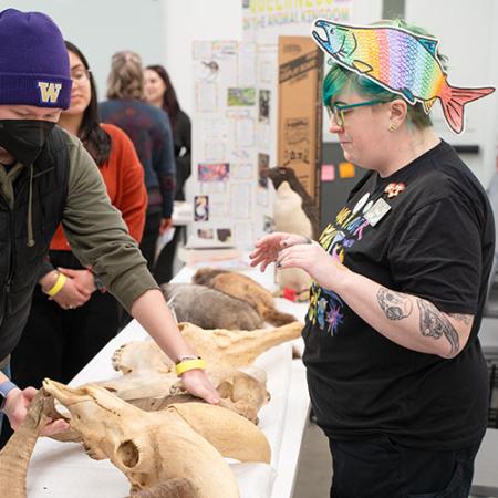 Wearing a rainbow-colored salmon hat, a Burke employee displays skulls on a table to a visitor