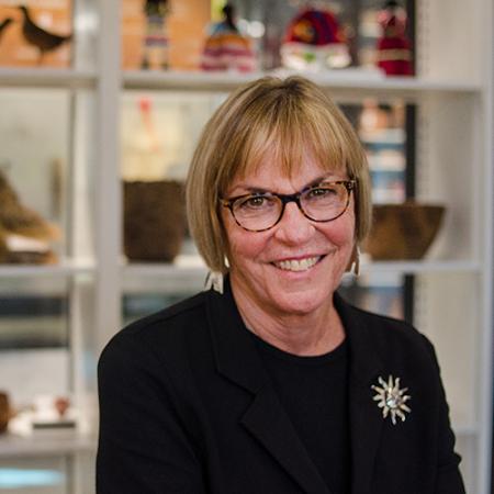 A woman smiles at the camera with museum collections on shelves behind her