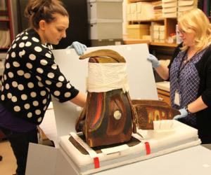 Two woman carefully unpack the native art mask from a box