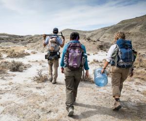 Three people with backpacks and palentology equipment walking in the desert